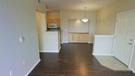 This single-floor residence offers a thoughtfully designed open-concept layout that seamlessly connects the main living, dining, and kitchen areas. Rich, dark hardwood flooring runs throughout, providing a warm and grounding contrast to the light-toned walls and cabinetry.

The kitchen is positioned off the main living space and features light wood cabinetry, a dark tile backsplash, and modern appliances including a microwave and range. A raised countertop bar creates a natural division between the kitchen and the living area, offering additional surface space and casual seating potential.

Adjacent to the kitchen, a dedicated dining area is defined by a stylish pendant light that hangs above the space, casting a warm, focused glow. Built-in cabinetry with a countertop surface lines the wall, offering both storage and display functionality — a distinctive architectural feature that adds character and practicality to the dining zone.

The open living area is generous in scale, allowing for flexible furniture arrangements. Neutral wall tones throughout create a clean, versatile backdrop that complements a variety of interior styles. The overall ambiance is calm and understated, with a layout that prioritizes open flow and functional living across every area of the home.