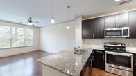 Located at 2025 Barrett Lakes Blvd NW in Kennesaw, Georgia, this one-bedroom, one-bathroom residence offers a well-designed single-floor layout that maximizes functionality and comfort. The open-concept kitchen and living area serves as the heart of the home, highlighted by rich dark cabinetry, granite countertops, a peninsula island with an undermount sink, stainless steel appliances including a range, microwave, and refrigerator, and a tile backsplash. Sleek pendant lighting and track lighting illuminate the kitchen, while a ceiling fan keeps the living area comfortable. Hardwood-style flooring flows throughout the main living spaces, adding warmth and continuity. Large windows throughout the unit invite generous natural light and offer views of surrounding greenery. The bedroom features plush carpeting, a ceiling fan, and a well-sized window with outdoor views. The bathroom is finished with a granite-top dark vanity, tile flooring, and a tub-shower combination. A dedicated laundry area with wire shelving provides added convenience. A private entry door with sidelight and transom window completes this thoughtfully appointed residence.