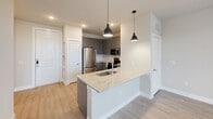 This single-story unit in Austin, Texas offers a thoughtfully designed open-concept layout that seamlessly connects the kitchen, dining, and living areas. The kitchen is equipped with stainless steel appliances, including a refrigerator, range, microwave, and dishwasher, all complemented by gray shaker-style cabinetry and a light granite-topped peninsula with an integrated sink. Black pendant lights above the peninsula add a modern touch, while light wood-look flooring extends throughout the main living areas.

The living space benefits from natural light streaming through multiple windows and a glass door that opens to a private outdoor area, with a ceiling fan overhead providing added comfort. Neutral-toned walls throughout the unit create a clean, cohesive aesthetic.

The bedroom is carpeted for warmth and comfort, featuring multiple windows, a ceiling fan, and access to a spacious walk-in closet outfitted with multiple hanging rods and shelving. The bathroom includes a gray vanity with granite countertops, a tub-shower combination, tile flooring, and ample cabinet storage, maintaining the same refined, contemporary style found throughout the unit.