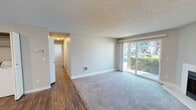 Located at 11328 SE Kent Kangley Rd in Kent, Washington, this single-story ground-floor unit offers a practical and well-organized layout. The living room serves as the central gathering space, featuring soft carpeting, a white-surround fireplace, and a large sliding glass door that fills the room with natural light and provides direct access to the outdoors. Neutral-toned walls and a textured ceiling are consistent throughout the unit.

The kitchen is equipped with white cabinetry, white appliances including a range and refrigerator, a dishwasher, and light stone-finish countertops. A double-basin stainless steel sink sits beneath a window, and wood-style flooring runs throughout the kitchen and connecting areas.

Two bedrooms offer carpeted floors, windows with blinds for natural light, and baseboard heating. Each room provides a quiet and functional space. The unit includes two bathrooms: one featuring a tub/shower combination with white surrounds, a single-sink vanity with white cabinetry, and wood-style flooring; the second is a half-bath style with a mirrored medicine cabinet and similar clean finishes. A hallway connects the main living areas to the private quarters, completing the straightforward and functional floor plan.