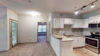 This single-floor residence offers a thoughtfully designed layout that balances functionality and comfort. The open-concept kitchen is a standout feature, showcasing granite countertops, white shaker-style cabinetry, a gray subway tile backsplash, stainless steel appliances including a refrigerator, range, and microwave, and a double-basin stainless steel sink. A peninsula counter with additional seating extends into the living area, creating a natural transition between the kitchen and the main living space. The living area is carpeted and well-lit, with track lighting accenting the kitchen zone and a view into the bedroom beyond. The bedrooms are generously sized, each featuring plush carpet flooring, ceiling fans with integrated lighting, and windows that frame views of lush, tree-lined surroundings. Natural light flows freely through the large windows, enhanced by blinds for privacy control. The bathroom is clean and functional, with wood-look tile flooring, a tiled tub-shower combination, granite vanity countertop, and chrome fixtures. Throughout the unit, neutral tones and textured ceilings create a cohesive, understated aesthetic well-suited for comfortable everyday living.