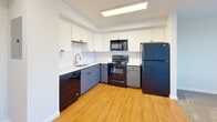 Located at 9503 State Rd in Philadelphia's 19114 neighborhood, this two-bedroom, one-bathroom unit offers a practical and well-organized single-floor layout. The kitchen is a standout feature, showcasing warm hardwood flooring, two-tone cabinetry with white upper cabinets and slate-blue lower cabinets, white subway tile backsplash, and a full suite of black appliances including a dishwasher, electric range, microwave, and refrigerator. A stainless steel sink and ample counter space complete the functional cooking area. Both bedrooms feature neutral-toned carpet flooring and light gray walls, creating a calm and versatile backdrop. The spacious primary bedroom receives natural light through a window fitted with blinds, while the second bedroom also benefits from natural light and offers direct sightlines to the kitchen. A carpeted hallway connects the bedrooms and provides access to closet storage as well as the full bathroom. The bathroom is finished with light tile flooring, a modern dark-toned vanity with an integrated sink, and a tub and shower combination with tile surround. Clean white walls throughout the unit lend a bright, cohesive feel to the entire space.