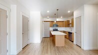 This single-floor residence offers a clean, modern aesthetic defined by light wood-look flooring, white walls, and an open layout that promotes a sense of airiness throughout. The kitchen serves as the heart of the home, showcasing warm wood cabinetry, a classic subway tile backsplash, and a suite of stainless steel appliances including a range, microwave, and dishwasher. A central island with a crisp white countertop provides additional prep space and casual seating, while two pendant lights hang above, adding a stylish finishing touch. Recessed lighting and an open sightline to the rest of the living area enhance the kitchen's bright, welcoming atmosphere. The living area is generously proportioned, bathed in natural light from a large window and a glass-paneled exterior door, with a ceiling fan overhead for added comfort. The bedroom is a calm, well-lit space with access to a full bathroom featuring a soaking tub and shower combination. A spacious walk-in closet with dual hanging rods and built-in shelving offers ample storage. A dedicated laundry room accommodates a full-size washer and dryer, complemented by overhead shelving. The entire unit presents a fresh, move-in ready condition throughout.