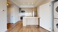 This modern 2-bedroom, 2-bathroom high-rise unit offers a thoughtfully designed open-concept layout with contemporary finishes throughout. The combined kitchen and living area serves as the heart of the home, featuring light wood cabinetry, stainless steel appliances, a built-in microwave, and a sleek white quartz peninsula with integrated shelving — ideal for dining or casual entertaining. Track lighting illuminates the space, which flows seamlessly onto warm hardwood-style flooring found throughout the unit. An in-suite stacked washer and dryer is conveniently tucked behind a closet door off the main living area. Floor-to-ceiling windows and sliding glass doors in both the living room and bedrooms flood the unit with natural light and frame sweeping panoramic views of the city skyline and waterfront. The primary bedroom includes mirrored sliding closet doors and access to city views, while a separate walk-in closet with wire shelving provides ample storage. Both bathrooms are finished with light wood floating vanities, white subway tile, large-format floor tile, and chrome fixtures — one featuring a soaking tub and the other a glass-enclosed shower. The overall ambiance is clean, bright, and contemporary, with a cohesive neutral palette throughout.
