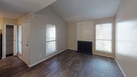 This single-floor unit offers a well-organized layout with a consistent design language throughout. The living room serves as the focal point, featuring vaulted ceilings that add a sense of openness, a classic wood-panel fireplace framed by two large windows that flood the space with natural light, and rich, dark hardwood-style flooring that runs throughout most of the unit.

The kitchen is efficiently designed in a galley configuration, with white cabinetry, granite-look countertops, and appliances including an electric range and dishwasher. Adjacent to the kitchen, a hallway benefits from a skylight overhead, brightening the transition spaces, and includes a louvered closet door for additional storage. A built-in countertop or desk surface is also present in this area, offering a functional workspace or utility niche.

The bedroom is comfortably sized, featuring a ceiling fan with integrated lighting, a window for natural light and ventilation, and a textured ceiling. It connects directly to a walk-in closet, illuminated by its own window and overhead lighting, providing ample storage.

The bathroom is clean and practical, appointed with white vanity cabinetry, granite-look countertops, a large vanity mirror with a lighted fixture above, and standard fixtures. The textured walls and consistent neutral palette give the entire unit a cohesive, understated aesthetic.