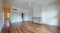 This single-floor space combines classic architectural character with modern updates throughout its well-appointed rooms. The main living area is a standout, showcasing rich, warm-toned hardwood flooring that runs the length of the room, soaring vaulted ceilings fitted with a ceiling fan, and a striking decorative fireplace framed by an elegant arched marble surround — a true focal point of the space. Built-in closet storage and an open flow to adjacent rooms add to the functionality of this area.

The bedroom features plush wall-to-wall carpeting and is bathed in natural light through multiple large windows with classic molding detail, offering views of the surrounding brick exterior streetscape. The windows contribute to the bright, airy atmosphere of the room.

The kitchen is equipped with rich cherry wood cabinetry, dark granite countertops, stainless steel appliances including a range, over-the-range microwave, and a sink with a modern faucet. Light tile flooring completes the clean, functional aesthetic.

The bathroom mirrors the kitchen's design sensibility, featuring the same cherry wood vanity with dark granite countertops, a large mirror, globe vanity lighting, tile flooring, and a combined tub and shower. Together, these spaces form a cohesive and well-maintained interior full of character.