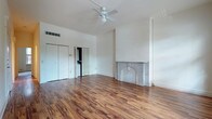 This single-floor space combines classic architectural character with modern updates throughout its well-appointed rooms. The main living area is a standout, showcasing rich, warm-toned hardwood flooring that runs the length of the room, soaring vaulted ceilings fitted with a ceiling fan, and a striking decorative fireplace framed by an elegant arched marble surround — a true focal point of the space. Built-in closet storage and an open flow to adjacent rooms add to the functionality of this area.

The bedroom features plush wall-to-wall carpeting and is bathed in natural light through multiple large windows with classic molding detail, offering views of the surrounding brick exterior streetscape. The windows contribute to the bright, airy atmosphere of the room.

The kitchen is equipped with rich cherry wood cabinetry, dark granite countertops, stainless steel appliances including a range, over-the-range microwave, and a sink with a modern faucet. Light tile flooring completes the clean, functional aesthetic.

The bathroom mirrors the kitchen's design sensibility, featuring the same cherry wood vanity with dark granite countertops, a large mirror, globe vanity lighting, tile flooring, and a combined tub and shower. Together, these spaces form a cohesive and well-maintained interior full of character.