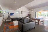 Located at 1785 Almaden Road in San Jose, CA, this single-floor space offers a sleek, modern open-plan layout that seamlessly integrates a fully equipped kitchen with a spacious living area. The interior is defined by crisp white walls, soaring vaulted ceilings, and polished concrete floors that lend the space an industrial-contemporary aesthetic. Natural light flows generously throughout, enhanced by large folding glass doors that open directly to an outdoor patio, blurring the line between interior and exterior. The kitchen is well-appointed with stainless steel appliances, including a full-size refrigerator, electric range, and ventilation hood, complemented by marble-patterned countertops and clean white tile backsplash. A high-top dining table with stools provides a casual seating area adjacent to the kitchen. The living area is furnished with tufted leather sofas arranged around a colorful area rug, with a large wall-mounted display screen and curated photographic artwork adorning the walls. A full-size pool table serves as a centerpiece recreational feature. A wall-mounted mini-split system ensures climate control throughout. A dedicated hallway with billiard cue storage and posted guidelines adds functional structure to the space.