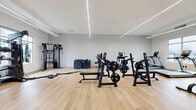 Located at 1685 Athena Dr in Kent, Ohio, this fitness facility offers a generously sized, single-floor workout space designed to accommodate a comprehensive range of exercise activities. The interior is finished with light wood-toned flooring throughout, contributing to a clean, modern aesthetic that is both functional and visually open.

The facility is illuminated by recessed linear LED lighting strips that run across the white ceiling, providing consistent, bright light across the entire floor. Ceiling fans assist with air circulation, and multiple windows along the perimeter walls allow natural light to enter while offering views of the surrounding outdoor environment.

The equipment layout is thoughtfully organized to maximize usable floor space. A dedicated strength training area includes plate-loaded machines, weight benches, and a cable functional trainer. A free weights section features a full rack of dumbbells, kettlebells, medicine balls, and stability balls. Cardio equipment, including treadmills and a rowing machine, is positioned near the windows. Battle ropes and plyo boxes add functional training options.

The entry area features light wood flooring, wall-mounted speakers, and a glass-paneled door that connects to an adjacent space. The overall ambiance is bright, clean, and purpose-built for fitness use.