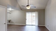 This single-story, 2-bedroom, 2-bathroom residence in Columbia, SC offers a functional and comfortable layout with notable architectural details. The living room is the centerpiece of the home, showcasing dramatic vaulted ceilings that lend an open, airy feel to the space. Rich hardwood-style flooring runs throughout, complemented by neutral-toned walls. A ceiling fan with a light fixture hangs from the peak of the vault, and a sliding glass door fitted with vertical blinds opens to an outdoor patio, allowing natural light to pour in. The kitchen features white cabinetry, light countertops, and black appliances including a range and dishwasher, all set above speckled flooring for a clean, classic look. The two bedrooms offer a quieter retreat; the primary bedroom is generously sized, while the second bedroom features plush carpeting and a window with blinds that brings in natural light. The bathrooms include a jetted soaking tub and shower combination, providing a spa-like touch. Two hallways connect the rooms efficiently, rounding out a practical and well-appointed floor plan suited for comfortable everyday living.