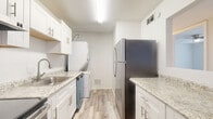 Located at 1831 13th Ave E in Bradenton, Florida, this refreshed single-floor residence offers a clean, modern aesthetic throughout. The open living area is bathed in natural light from a large picture window, complemented by light-toned luxury vinyl plank flooring that extends seamlessly through the space. A ceiling fan adds both style and comfort to the generous living room, which connects effortlessly to the rest of the unit.

The galley-style kitchen is well-appointed with crisp white shaker cabinetry, granite-look countertops, a stainless steel sink, and a full suite of stainless steel appliances including a refrigerator, electric range, and dishwasher. A stacked washer and dryer unit is conveniently integrated into the kitchen area, adding practical in-unit laundry functionality.

The bedrooms feature the same light wood-look flooring, neutral walls, and natural light from windows with blinds. One bedroom includes a ceiling fan and another offers a sliding closet for additional storage.

The bathroom is tastefully finished with marble-look tile flooring, large-format tile surrounding the tub and shower, a sleek glass shower door, and a white vanity. The overall design is clean, neutral, and move-in ready, making this Bradenton residence a functional and attractive living space.