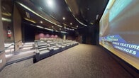 Located in West Palm Beach, Florida, this dedicated private screening room delivers a true cinematic experience within a generously sized, single-floor layout. The space is defined by its dramatic architectural design, featuring a sweeping, curved ceiling with layered panels that create a dynamic overhead aesthetic. Recessed and cove lighting is strategically positioned throughout, casting a warm, ambient glow that enhances the immersive atmosphere.

The seating arrangement consists of multiple rows of premium, oversized reclining chairs upholstered in both gray and cream leather, positioned on a gently tiered floor to ensure unobstructed sightlines from every seat. The large-format projection screen dominates the front wall, providing an expansive and high-impact viewing surface suited for professional presentations, private screenings, or entertainment events.

Dark, acoustically treated wall panels line the perimeter, contributing to optimal sound quality while reinforcing the room's refined, theater-like ambiance. Plush carpeting covers the floors throughout, adding comfort underfoot and further supporting acoustic performance. A central aisle provides clear access to all seating areas, and a dedicated entry door with emergency exit signage ensures safety compliance. The overall design is sleek, modern, and purpose-built for an elevated viewing experience.