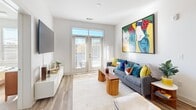 Located at 145 New Bern St in Charlotte, NC, this two-bedroom, two-bathroom residence offers a thoughtfully designed single-floor layout that maximizes every square foot. The open-concept kitchen features gray shaker-style cabinetry, stainless steel appliances including a range, microwave, and refrigerator, light quartz countertops, and a central island with pendant lighting — ideal for both meal prep and casual dining. Warm hardwood-style flooring flows through the kitchen and into the living area. The living room is bright and inviting, anchored by French doors with transom windows that fill the space with natural light and provide outdoor access. Two carpet-lined bedrooms offer a quiet retreat; the primary bedroom is generously sized and features a ceiling fan, large windows, and an en-suite bathroom with a glass-enclosed shower, dual vanity, and walk-in closet. The second bedroom is bright and well-proportioned, served by a full hallway bathroom with a shower-tub combo and tile flooring. Two dedicated closets provide ample storage throughout. Clean white walls, modern finishes, and a neutral palette create a cohesive, contemporary ambiance throughout this Charlotte residence.