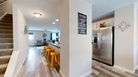 This two-story home offers a thoughtfully designed layout that balances functionality and comfort across both levels. The main floor showcases an open-concept living space anchored by light wood-look flooring that flows seamlessly throughout. The kitchen is equipped with stainless steel appliances, white cabinetry, dark countertops, and a central island with bar seating, making it a practical and social hub. Recessed lighting and natural light from multiple windows keep the space bright and welcoming. The kitchen opens directly into the spacious living room, which features a ceiling fan, large windows with blue draping curtains, and ample room for seating. A dedicated dining area accommodates a substantial dark wood dining table set beneath a window, adding an inviting atmosphere for gatherings. The bedrooms are generously sized with plush carpeting and ceiling fans. The primary bedroom provides a calm, restful retreat, while a secondary bedroom is configured with a loft bed, offering a creative and functional setup. The bathrooms are clean and efficiently designed, featuring a walk-in shower with white subway tile. Throughout the home, neutral tones and consistent finishes create a cohesive and comfortable living environment well-suited for everyday living.