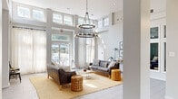 Located at 1235 Ashbourne Rd in Elkins Park, PA, this thoughtfully designed single-floor space offers a welcoming and versatile environment across four distinct areas. The centerpiece is a grand lounge boasting soaring double-height ceilings adorned with a striking two-tiered wrought-iron chandelier. Floor-to-ceiling windows and transom windows flood the room with abundant natural light, while glass French doors open to an outdoor area, seamlessly blending interior and exterior spaces. Rich leather sofas, woven jute rugs, and wooden accent stools lend a warm, contemporary aesthetic throughout. An adjacent lounge area provides a more intimate setting with lighter furnishings, a round mirror, and layered window treatments that diffuse soft, even light. A dedicated meeting and collaborative workspace features a solid wood communal table, modern task seating, decorative wall art, and built-in printer access — ideal for productive gatherings. A compact kitchenette serves the space with white cabinetry, butcher block countertops, and built-in appliances. Light tile flooring runs consistently throughout, unifying the layout. The overall ambiance is modern yet inviting, combining clean architectural lines with carefully curated furnishings to create a functional and aesthetically refined environment.