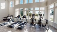 Located at 9124 Charlotte Hwy in Fort Mill, SC, this well-appointed fitness center is designed to support a wide variety of workout routines in a bright, open environment. The space is defined by its dramatically high ceilings, which are fitted with large ceiling fans to promote air circulation throughout. Expansive floor-to-ceiling windows line multiple walls, flooding the interior with natural light and offering pleasant outdoor views of the surrounding landscape.

The main workout floor features durable wood-look flooring and houses an extensive selection of strength training equipment, including cable machines, weight benches, a stair climber, a rowing machine, and a rack of kettlebells arranged along a mirrored wall. A dedicated cardio zone is equipped with multiple treadmills, elliptical trainers, and upright exercise bikes positioned directly in front of the large window banks.

A separate spin studio provides a quieter, focused cycling experience with interactive screen-equipped bikes. Additionally, a mirrored studio area features a wall-mounted display screen and an assortment of functional training accessories, including stability balls and resistance tools, making it suitable for group classes or individual exercise sessions. The overall ambiance is clean, modern, and energizing.
