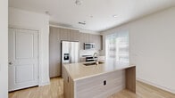 Located at 1933 S Acoma St in Denver's Baker neighborhood, this single-story residence showcases a clean, modern design with a cohesive neutral palette and light wood-look flooring throughout. The open-concept kitchen is a standout feature, equipped with flat-front cabinetry in a warm wood-grain finish, a spacious center island with an integrated sink and light quartz countertops, and a full suite of stainless steel appliances including a side-by-side refrigerator with ice maker, a built-in microwave, and an electric range. A bright window with horizontal blinds allows natural light to fill the space. The layout flows seamlessly from the kitchen into the living areas, which benefit from multiple large windows that invite abundant natural light and views of the surrounding neighborhood. The bedrooms are well-proportioned, each featuring light wood flooring, generous windows with blinds, and clean white walls — one bedroom includes a ceiling fan. The bathroom features marble-look tile flooring, a wood-tone vanity cabinet, and direct access to a walk-in closet. The overall design emphasizes minimalism and functionality, creating a bright and inviting environment throughout.