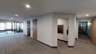 This single-floor common area space is thoughtfully designed to serve the practical and social needs of its occupants. The entrance corridor is clean and functional, finished with neutral carpet flooring and crisp white walls. The hallway provides direct access to an elevator, a wood-paneled door, and a dedicated mailroom alcove housing a full bank of individual metal mailboxes framed in warm wood trim.

The kitchen is a standout feature of the space, outfitted with rich dark espresso cabinetry that extends to the ceiling, complemented by light granite countertops and tile flooring. Stainless steel appliances — including a full-size refrigerator, electric range with a hood vent, dishwasher, and microwave — provide a fully functional cooking and gathering environment. A double sink rounds out the well-appointed kitchen layout.

Adjacent to the kitchen is an open multipurpose area with additional cabinetry and counter space, offering flexibility for dining or lounge use. This area features a large window fitted with horizontal blinds, allowing natural light to filter in while providing views of the surrounding neighborhood. The drop-panel ceiling with flush lighting fixtures maintains a clean, professional aesthetic throughout. Overall, the space delivers a practical, welcoming environment suitable for community gatherings and everyday use.