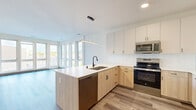 Located at 1659 N Jackson St in Milwaukee's vibrant lower east side, this contemporary one-bedroom unit offers a thoughtfully designed single-floor layout with modern finishes throughout. The open-concept kitchen and living area serves as the heart of the space, featuring warm wood-toned lower cabinetry paired with crisp white upper cabinets, a white quartz peninsula with an undermount sink, subway tile backsplash, and a full suite of stainless steel appliances including a refrigerator, electric range, microwave, and dishwasher. A sleek linear pendant light anchors the kitchen, while large floor-to-ceiling windows and a sliding glass door flood the living area with natural light and provide direct access to a private balcony with outdoor views. Light wood-toned LVP flooring runs throughout the main living areas, complementing the clean, neutral palette. The well-proportioned bedroom offers plush carpet, generous window coverage, and access to a walk-in closet with adjustable wire shelving. The bathroom is finished with a wood-toned vanity, white quartz countertop, matte black hardware, and a glass-enclosed shower. Additional conveniences include a dedicated laundry area, utility room, and a second closet for extra storage.