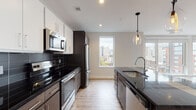 Located at 95 St Alphonsus St in Boston's Mission Hill neighborhood, this modern single-floor residence offers a thoughtfully designed layout with contemporary finishes throughout. The open-concept kitchen is a standout feature, equipped with stainless steel appliances, dark granite countertops, a contrasting two-tone cabinet scheme of white upper and dark lower cabinetry, a sleek subway tile backsplash, and an island with pendant lighting. Windows frame views of the Boston skyline, bringing natural light into the cooking and dining area. The living space is bright and expansive, featuring light hardwood-style flooring and recessed lighting, with large windows offering additional city views. The bedrooms are well-proportioned and filled with natural light through generously sized windows overlooking the surrounding urban landscape. Each bathroom is finished with large-format tile flooring, dark wood vanities topped with quartz countertops, chrome fixtures, and glass-enclosed shower areas. The clean, neutral palette and modern design elements create a cohesive, contemporary ambiance throughout, making this a well-appointed urban residence in one of Boston's vibrant neighborhoods.