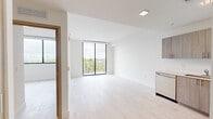 Located at 1601 SW 32nd Ave in Miami's vibrant Little Havana neighborhood, this modern one-bedroom, one-bathroom residence offers a thoughtfully designed open floor plan bathed in natural light. Light-toned wood flooring runs throughout, complementing the clean white walls and contemporary finishes.

The combined kitchen and living area serves as the heart of the home. The kitchen features warm wood-toned cabinetry, light countertops, a stainless steel refrigerator, range, microwave, and dishwasher — providing a fully equipped, functional cooking space. The open living area flows seamlessly toward floor-to-ceiling sliding glass doors that lead to a private balcony, offering sweeping views of Miami's skyline framed by lush palm trees.

The bedroom is a well-proportioned retreat featuring large black-framed windows that frame the same stunning cityscape and tropical greenery. A built-in open closet system offers organized storage. The bathroom is finished in clean white tile with a full soaking tub and shower combination.

Throughout the residence, recessed lighting and large windows ensure a bright, airy ambiance. Modern interior doors with wood accents add warmth, rounding out this well-appointed urban home in the heart of Miami.