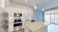 Located at 6300 Clayton Ave in St. Louis, Missouri, this modern single-floor residence offers a thoughtfully designed layout with contemporary finishes throughout. The kitchen serves as a standout centerpiece, featuring crisp white shaker cabinetry extending to the ceiling for ample storage, light granite countertops with subtle veining, a classic white subway tile backsplash, and a full suite of stainless steel appliances including a range, microwave, dishwasher, and refrigerator. A generously sized island provides additional prep and seating space, while elegant glass pendant lights overhead add a refined touch. The living area is bathed in natural light through a full-height sliding glass door that opens to a private balcony, complemented by durable wood-look flooring that flows throughout the unit. The bedroom is a calm, neutral retreat with large windows and the same warm flooring, offering a clean and versatile space. The bathroom is well-appointed with a glass-enclosed walk-in shower, granite-topped vanity with white cabinetry, and wood-look tile flooring that ties the space together cohesively. The overall aesthetic is clean, modern, and move-in ready.