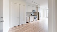 Located at 9 St. Stevens Court in Toronto, Ontario, this well-appointed one-bedroom, one-bathroom unit offers a thoughtfully designed open-concept layout with contemporary finishes throughout. Light oak laminate flooring runs seamlessly across the main living areas, complementing the crisp white walls and clean modern aesthetic.

The combined dining and kitchen area is equipped with a full suite of stainless steel appliances, including a refrigerator, stove, microwave, and dishwasher, set against white cabinetry that extends to the ceiling for ample storage. Track lighting above adds both functionality and a modern touch.

The living room is bright and airy, benefiting from floor-to-ceiling windows that invite generous natural light and provide views of the surrounding Toronto cityscape. A private balcony extends the living space outdoors. An additional den offers flexible use as a home office or secondary lounge area.

The bedroom features large windows with city views, warm laminate flooring, and a double-door closet providing practical storage. The bathroom is finished with marble-style porcelain floor tiles, a sleek white vanity with an undermount sink, a framed mirror, and a glass-enclosed shower with marble tile surround. Three closets throughout the unit ensure excellent storage capacity. A welcoming entrance with a bold blue door completes this modern Toronto residence.