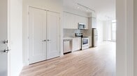 Located at 9 St. Stevens Court in Toronto, Ontario, this well-appointed one-bedroom, one-bathroom unit offers a thoughtfully designed open-concept layout with contemporary finishes throughout. Light oak laminate flooring runs seamlessly across the main living areas, complementing the crisp white walls and clean modern aesthetic.

The combined dining and kitchen area is equipped with a full suite of stainless steel appliances, including a refrigerator, stove, microwave, and dishwasher, set against white cabinetry that extends to the ceiling for ample storage. Track lighting above adds both functionality and a modern touch.

The living room is bright and airy, benefiting from floor-to-ceiling windows that invite generous natural light and provide views of the surrounding Toronto cityscape. A private balcony extends the living space outdoors. An additional den offers flexible use as a home office or secondary lounge area.

The bedroom features large windows with city views, warm laminate flooring, and a double-door closet providing practical storage. The bathroom is finished with marble-style porcelain floor tiles, a sleek white vanity with an undermount sink, a framed mirror, and a glass-enclosed shower with marble tile surround. Three closets throughout the unit ensure excellent storage capacity. A welcoming entrance with a bold blue door completes this modern Toronto residence.