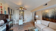 This single-floor residence offers a thoughtfully organized layout that balances comfort and functionality across its key living spaces. The living room serves as the central gathering area, featuring warm carpet flooring, a ceiling fan with lighting, and a sliding glass door that allows natural light to fill the space and provides access to an outdoor view. The open connection to the dining area, which accommodates a round glass table with modern white chairs, creates a seamless flow for everyday living and entertaining. The kitchen is designed with a galley-style configuration, featuring dark wood cabinetry, light countertops, tile flooring, and essential appliances including a refrigerator, dishwasher, and oven. The primary bedroom is a comfortable retreat with plush carpet, a textured ceiling, and windows that bring in natural light. A secondary bedroom offers a cheerful and versatile space, also carpeted and filled with natural light from multiple windows with blinds. The full bathroom is finished with warm earth-toned tile work surrounding a full soaking tub and shower combination, complemented by a large mirror and vanity. Throughout the residence, neutral wall tones and carpet flooring provide a cohesive and welcoming atmosphere.