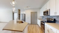 This well-appointed single-floor residence offers a thoughtfully designed open-concept layout that seamlessly connects the kitchen and living areas. The kitchen is a standout feature, showcasing crisp white cabinetry, a grey subway tile backsplash, stainless steel appliances — including a range, built-in microwave, and refrigerator — and a generous island with an undermount sink and pendant globe lighting overhead. Light hardwood flooring flows throughout the main living and kitchen areas, contributing to a bright, contemporary aesthetic.

The bedrooms are carpeted for comfort and feature ceiling fans, neutral toned walls, and windows that allow natural light and outdoor views to fill the space. The bathrooms are finished with large-format marble-style tile on both the floors and walls. The secondary bathroom includes a soaking tub with a tiled surround, while the primary bathroom offers a glass-enclosed walk-in shower, a dual-sink vanity with white cabinetry, and direct access to a walk-in closet. Together, these features create a clean, modern living environment with functional design and quality finishes throughout.