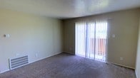This single-floor residential space offers a straightforward and functional layout designed for comfortable everyday living. The main living area is finished with wall-to-wall carpeting in a neutral tone, providing a warm and quiet underfoot experience. Smooth, light-colored walls complement the space throughout, contributing to a clean and understated aesthetic.

A prominent feature of the living area is the full-height sliding glass door dressed with vertical blinds, which allows for adjustable natural light throughout the day. The door opens to a balcony, offering a glimpse of the surrounding outdoor environment and providing a connection to the exterior. The textured ceiling adds a subtle visual detail consistent with classic residential construction.

The overall ambiance of the space is calm and neutral, offering a blank canvas well-suited for personalization. The absence of heavy architectural ornamentation keeps the focus on practicality and livability. Natural light filtering through the sliding door brightens the interior and enhances the sense of openness within the living area. This space presents a solid, no-frills residential option with comfortable foundational finishes and convenient outdoor access.