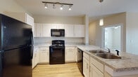 This single-floor residence offers a thoughtfully designed layout with a neutral color palette and a variety of flooring options that complement each living space. The kitchen is a functional centerpiece, featuring crisp white shaker-style cabinetry, granite-look countertops, and a full suite of black appliances including a gas range, over-the-range microwave, dishwasher, and refrigerator. A double-basin stainless steel sink anchors the kitchen island, while track lighting and a pendant light provide ample illumination. The living areas are finished with warm wood-look laminate flooring and ceiling fans, with windows fitted with horizontal blinds that allow for natural light. Bedrooms are carpeted for comfort, each offering closet storage and ceiling fans, creating a cozy and practical retreat. The hallway connects the rooms seamlessly, with recessed lighting and additional built-in storage visible along the corridor. The bathrooms are finished with wood-look vinyl flooring and include tiled tub/shower combinations with chrome fixtures, providing a clean and modern aesthetic. Overall, the space presents a well-balanced and move-in-ready interior suited for comfortable everyday living.