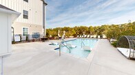 This pristine pool area in Calabash, NC, is a centerpiece of relaxation and leisure. The large, rectangular pool is lined with crystal-clear blue water, inviting guests for a refreshing swim. Surrounding the pool is an expansive concrete deck, perfect for sunbathing and socializing. Multiple lounge chairs and umbrellas are strategically placed around the pool, providing ample seating and shade options.

The pool area is nestled against a backdrop of lush pine trees, creating a serene and natural environment. This verdant setting not only enhances privacy but also offers a picturesque view for swimmers and sunbathers alike. The property features modern, multi-story white buildings with large windows, suggesting comfortable accommodations nearby.

Safety features include metal railings for easy pool access and a surrounding fence for security. The landscaping incorporates a mix of small trees, shrubs, and rock gardens, adding to the overall aesthetic appeal. An aerial view reveals the pool's generous size and its central location within the property complex.

This well-maintained facility appears to be part of a larger residential or resort property, offering residents or guests a high-quality outdoor recreation space. The combination of the inviting pool, comfortable amenities, and natural surroundings creates an ideal setting for relaxation and enjoyment in Calabash's pleasant climate.