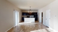 This two-story home is designed with a practical and modern aesthetic, centered around an open-concept main level that seamlessly connects the living area and kitchen. The living space is generously sized, featuring warm wood-look flooring that extends throughout and a striking chandelier with exposed Edison bulbs as a focal point. Large sliding glass doors and windows allow abundant natural light to pour in, brightening the neutral-toned walls and creating an airy atmosphere.

The kitchen is a standout feature of the main level, equipped with dark espresso cabinetry that reaches toward the ceiling, granite-look countertops, and a full suite of black appliances including a range, over-the-range microwave, and refrigerator. A central island with a sink adds functionality and serves as a natural gathering point. Track lighting complements the island chandelier overhead.

A dedicated laundry area includes a full-size top-loading washer and dryer set by Whirlpool, paired with dark overhead cabinetry and a wall-mounted drying rack for added convenience.

The bathroom features a dark vanity with granite countertops, a large mirror, and a walk-in shower with clean white surround panels and chrome fixtures. The upper floor is accessed via a staircase with a white railing, leading to a landing with wood-look flooring and additional rooms.