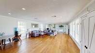 Located at 11850 Wentling Ave in Baton Rouge, Louisiana, this single-story space offers a thoughtfully designed layout that balances functionality and comfort. Warm hardwood flooring flows throughout the main areas, complemented by neutral gray walls, crown molding, and a textured ceiling with recessed lighting that creates a clean, welcoming ambiance.

The open living room is bright and inviting, featuring large windows that flood the space with natural light and offer views of an outdoor pool and patio area. A wall-mounted flat-screen TV, comfortable seating, and a small coffee station make this area well-suited for both relaxation and professional gatherings.

The kitchen is efficiently designed with white cabinetry, granite-style countertops, a peninsula breakfast bar, a full-size refrigerator, and a sink. It is well-equipped for everyday use and connects seamlessly to the main living area.

A dedicated private office, enclosed with glass-panel walls, provides a semi-transparent workspace fitted with a ceiling fan, desk, office chairs, and filing storage—ideal for focused work or client meetings.

The entrance area is open and functional, with durable tile flooring and direct sightlines into the main living space. Abundant natural light from multiple windows and a glazed front door enhances the airy feel throughout. Views of the adjacent pool area add a distinctive outdoor dimension to this versatile Baton Rouge property.