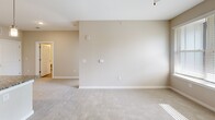 Located at 15118 Flagpole Dr, Unit 303 in Charlotte, NC, this one-bedroom, one-bathroom residence offers a well-designed open floor plan that maximizes its comfortable footprint. The kitchen is a standout feature, showcasing white shaker-style cabinetry, granite countertops, a tile backsplash, and a full suite of stainless steel appliances including a French door refrigerator, electric range, microwave, and dishwasher. A central kitchen island with a granite top and undermount sink provides additional prep space and casual dining potential, accented by three pendant lights overhead. Wood-look flooring runs throughout the kitchen and entry areas, transitioning to plush carpet in the open living space and bedroom. The living area is bright and open, offering a clean neutral palette and a ceiling fan. The bedroom is a well-proportioned retreat featuring a ceiling fan, natural light from a window with blinds, and direct access to the bathroom. The full bathroom features matching granite countertops, white cabinetry, and wood-look flooring. A dedicated closet provides ample storage. The overall design is modern and cohesive, with consistent finishes and a light, airy ambiance throughout.