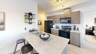 Located at 409 E Hills Blvd SE in Calgary, Alberta, this 2-bedroom, 2-bathroom unit offers a thoughtfully designed single-level layout that maximizes every square foot. The entrance leads into a bright, clean hallway finished with light wood-look flooring and crisp white walls, setting a modern and welcoming tone throughout.

The open-concept kitchen and dining area serve as the heart of the home. The kitchen features medium-toned wood cabinetry, light stone countertops, a white subway tile backsplash, and full black appliance suite including a refrigerator, electric range, and over-range microwave. A peninsula counter provides additional prep space and casual seating. The adjoining dining area is framed by a large window that brings in natural light, creating an airy atmosphere ideal for everyday meals.

The living room is comfortably sized with a large window overlooking the street, light flooring, and a neutral palette that suits a range of décor styles. Both bedrooms are well-proportioned, with the primary bedroom offering a comfortable retreat. The second bedroom also features a bright window and light carpet. Each of the two bathrooms is finished in clean white tile; one includes a glass-enclosed walk-in shower. Throughout the unit, the consistent use of light tones and modern finishes creates a cohesive, contemporary living environment.