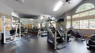 Located at 2727 Nelson Rd in Longmont, Colorado, this fitness center offers a comprehensive workout environment within a single, open-plan room. The space is defined by its vaulted ceilings, which lend a sense of airiness and openness, and are complemented by ceiling fans that help maintain comfortable airflow during workouts. Large windows with wood-trimmed frames and decorative valances line the walls, allowing abundant natural light to filter in while providing views of the surrounding greenery.

The interior features dark rubber flooring suited for heavy equipment use, and a full wall of mirrors that visually expands the space and allows users to monitor their form. The equipment selection is varied and includes cardio machines such as stair climbers, stationary bikes, and ellipticals, as well as a multi-station cable strength machine and a dumbbell rack with a full range of free weights. A wall-mounted television provides entertainment during workouts.

Overhead fluorescent lighting supplements the natural light, ensuring the space remains well-lit at all times. A bulletin board and informational postings are visible near the entrance, and a wall-mounted TV adds convenience. The overall ambiance is functional yet welcoming, making this fitness center a practical amenity for residents of the Longmont community.