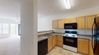 Located at 2792 Stantonsburg Rd in Greenville, NC, this single-floor unit offers a well-organized, open-concept layout designed for comfortable everyday living. The kitchen is a functional centerpiece, featuring light maple cabinetry with ample upper and lower storage, a double-basin sink, a full suite of black appliances including a refrigerator, range, over-the-range microwave, and dishwasher, all set atop durable tile flooring. A breakfast bar counter separates the kitchen from the living area, and a decorative column adds a subtle architectural touch. The living area is generously sized with soft wall-to-wall carpeting and a ceiling fan with light fixture overhead. Bedrooms continue the carpeted flooring theme, offering comfortable, neutral spaces. One bedroom benefits from natural light through a window with blinds and includes its own ceiling fan, while another features access to a walk-in closet, providing excellent storage. The bathrooms are finished with warm tile flooring and include a soaking tub, toilet, vanity with cabinetry, and towel bars. Throughout the unit, textured ceilings, neutral wall tones, and clean white trim create a bright, cohesive aesthetic.