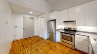 Located at 95 Chestnut St in Providence, Rhode Island, this one-bedroom, one-bathroom loft-style unit blends industrial character with modern updates. Warm hardwood floors run throughout the entire space, complementing the soaring ceilings and open feel. The kitchen is well-appointed with white shaker cabinetry, dark granite-style countertops, and a full suite of stainless steel appliances including a refrigerator, electric range, and dishwasher — all set against clean white walls that brighten the space. The living area opens to an impressive wall of large, black-framed industrial windows set above original exposed brick, flooding the room with natural light and offering views of the surrounding Providence neighborhood. Pendant lighting and exposed ductwork add to the loft aesthetic throughout. The bedroom is a comfortable size, featuring the same rich hardwood floors and a closet for storage. The bathroom is finished with classic white subway tile in the tub surround, a white vanity with under-cabinet storage, and tile flooring, giving it a clean and timeless look. This unit offers a distinctive urban living experience rooted in Providence's architectural heritage.