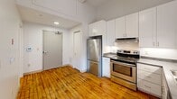 Located at 95 Chestnut St in Providence, Rhode Island, this one-bedroom, one-bathroom loft-style unit blends industrial character with modern updates. Warm hardwood floors run throughout the entire space, complementing the soaring ceilings and open feel. The kitchen is well-appointed with white shaker cabinetry, dark granite-style countertops, and a full suite of stainless steel appliances including a refrigerator, electric range, and dishwasher — all set against clean white walls that brighten the space. The living area opens to an impressive wall of large, black-framed industrial windows set above original exposed brick, flooding the room with natural light and offering views of the surrounding Providence neighborhood. Pendant lighting and exposed ductwork add to the loft aesthetic throughout. The bedroom is a comfortable size, featuring the same rich hardwood floors and a closet for storage. The bathroom is finished with classic white subway tile in the tub surround, a white vanity with under-cabinet storage, and tile flooring, giving it a clean and timeless look. This unit offers a distinctive urban living experience rooted in Providence's architectural heritage.