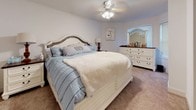 This thoughtfully designed two-bedroom, two-bathroom Virginia residence offers a comfortable and functional single-floor layout. The living room is a standout space, anchored by a sweeping bay window that fills the room with natural light, complemented by crown molding and a ceiling fan. A dedicated dining area features its own window with outdoor views, creating an inviting setting for meals. The kitchen is well-equipped with light wood cabinetry, dark granite countertops, tile flooring, and a full suite of stainless steel appliances including a range, microwave, and refrigerator. The primary bedroom is generously sized with plush carpeting, a ceiling fan, and a matching dresser suite, leading to a spa-like en-suite bathroom boasting a tiled soaking tub positioned beneath a bay window, a separate glass-enclosed shower, and tile flooring. The second bedroom is equally comfortable, featuring a charming built-in window seat with views, soft carpeting, and a stylish whitewashed bed frame. The second bathroom includes a shower/tub combination, wood cabinetry with overhead storage, and tile surround. Throughout, the home maintains a warm, neutral palette with consistent attention to detail.