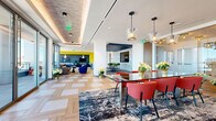 Located at 401 S. Graham Street in Charlotte, NC, this sophisticated amenity lounge offers a thoughtfully designed, open-plan layout spanning a generously proportioned single floor. The space is defined by its striking geometric herringbone and parquet-patterned hardwood flooring, which flows seamlessly throughout each functional zone.

Floor-to-ceiling glass curtain walls dominate multiple sides of the space, flooding the interior with abundant natural light and framing sweeping panoramic views of the Charlotte skyline and surrounding cityscape. A large lounge area anchors one end, furnished with a substantial leather sectional sofa positioned to maximize the dramatic outlook.

The dining and social zone features a glass-top conference table surrounded by bold red chairs, suspended beneath elegant glass pendant lighting. Adjacent to this is a full-service kitchen corridor outfitted with contemporary gray cabinetry, white countertops, subway tile backsplash, built-in appliances, and large planters with live greenery.

A bar area with yellow velvet barstools and gold accents adds a vibrant focal point, while a separate media nook with bold yellow and blue walls offers an energetic retreat. A mosaic-tiled wet bar with green counter seating provides additional social space. The overall ambiance is modern, vibrant, and professionally curated.