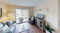 This single-floor residence offers a thoughtfully laid-out living space with a warm, neutral color palette that creates a cohesive and inviting atmosphere throughout. The living room serves as the heart of the home, featuring durable wood-look flooring, a sliding glass door with vertical blinds that opens to an outdoor patio, and views of lush greenery beyond — filling the room with natural light. The space comfortably accommodates a seating arrangement and entertainment setup. Adjacent to the living room, the dining area provides an intimate setting with recessed lighting overhead and the same wood-look flooring, ideal for everyday meals. The galley-style kitchen is efficiently designed with warm oak cabinetry, a double-basin stainless steel sink, a full suite of black appliances including a range and refrigerator, and ample counter space for meal preparation. The bedroom is a serene retreat, finished with plush carpeting and centered around a ceiling fan with light fixture. Large sliding windows with vertical blinds invite natural light and outdoor views, complementing the room's restful ambiance. The bathroom features a full tub and shower combination with decorative tiled accents, completing this functional and comfortable residence.
