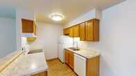 This single-floor residence offers a practical and comfortable layout designed for everyday living. The kitchen is outfitted with warm honey-toned oak cabinetry, light laminate countertops, and white appliances including a refrigerator and dishwasher. A double-basin sink sits beneath upper cabinets that provide ample storage, while light wood-look flooring ties the space together. The kitchen opens to a dining area via a half-wall breakfast bar, with a chandelier overhead adding a touch of character to the space.

The living room is generously sized with durable wood-look flooring, neutral walls, and a sliding glass door dressed with vertical blinds that allows natural light to fill the room. Baseboard heating units run along the walls, a consistent feature throughout the residence.

Multiple bedrooms feature plush neutral carpeting, windows with exterior views of mature trees, and warm wood-trimmed door frames. Each room is well-lit and offers a clean, understated aesthetic with ample wall space. One bedroom includes an attached closet for added convenience.

The bathroom features wood-look flooring, warm oak cabinetry with a white vanity top, and accessibility-conscious grab bars near the toilet and wall, making the space both practical and inclusive.