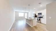 Located at 2918 W 29th Ave in Denver's vibrant West Highland neighborhood, this single-floor unit offers a thoughtfully designed open-concept layout with clean, contemporary finishes. Light hardwood flooring flows seamlessly throughout the entire space, enhancing the bright and airy atmosphere created by neutral walls and abundant natural light.

The kitchen and living area form the heart of the unit, centered around a large granite-topped island with a built-in sink and pendant lighting overhead. The kitchen is well-appointed with white shaker cabinetry extending to the ceiling, stainless steel appliances including a refrigerator, range, microwave, and dishwasher, and matching granite countertops. The open layout allows the kitchen to flow naturally into the living area, which features a window and exterior door that invite natural light and outdoor access.

A well-organized hallway connects the main living space to the bathroom and closet. The bathroom features light wood-look tile flooring, a white vanity with granite countertop and undermount sink, a framed mirror, and clean white fixtures. The closet provides convenient dedicated storage. A utility closet housing the water heater and mechanical systems is also accessible from the hallway. Recessed lighting and pendant fixtures complete this polished, move-in-ready space.