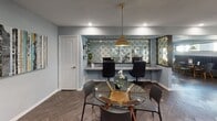 Located at 7510 Brompton St in Houston, TX, this thoughtfully designed single-floor amenity space blends recreation, productivity, and style into a cohesive environment. The layout is anchored by a spacious game room centered around a full-size billiard table beneath a contemporary globe pendant light. Herringbone-patterned wood flooring flows throughout, lending warmth and visual continuity across all areas. Natural light filters in through large windows and glass doors that open to the outdoors, creating an inviting, airy atmosphere.

The wet bar area is a standout feature, showcasing bold navy blue cabinetry accented with gold hardware and a sleek gray countertop that wraps along two walls in an L-shaped configuration. A stainless steel dishwasher is integrated seamlessly into the cabinetry, while a textured stone tile backsplash adds depth and character. Floating white shelves provide both display and storage space above the counter.

Adjacent to the main gathering area is a dedicated workspace designed for collaboration. A built-in dual-workstation desk faces a decorative gold-patterned accent wall, framed by mirrored panels that amplify light and space. A glass-top round table with seating sits at the center, suitable for meetings or casual gatherings. Soft blue-gray walls and recessed lighting throughout contribute to the space's calm, polished ambiance.