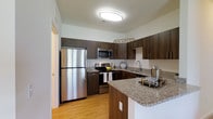 Located at 1150 Helen Drive in Newark, Delaware, this single-floor residence offers a thoughtfully designed living space with modern finishes throughout. The kitchen stands out as a centerpiece of the home, showcasing rich dark wood cabinetry that extends to the ceiling, providing ample storage and a sleek, contemporary aesthetic. Granite countertops with subtle speckled detailing run across the workspace and extend to a convenient breakfast bar, ideal for casual dining or entertaining. Stainless steel appliances, including a full-size refrigerator, range, and built-in microwave, lend a polished, professional quality to the kitchen. Warm hardwood-style flooring flows underfoot, complementing the darker cabinetry and creating a welcoming contrast. A dual-basin sink is positioned beneath a dedicated workspace area, maximizing functionality. The space is brightened by overhead flush-mount lighting, contributing to a clean and well-lit environment. The kitchen's open layout and peninsula-style counter arrangement promote an easy flow between cooking and living areas. Overall, the residence exudes a modern yet comfortable ambiance, combining practical design with attractive finishes that make everyday living both stylish and functional.