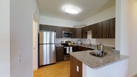 Located at 1150 Helen Drive in Newark, Delaware, this single-floor residence offers a thoughtfully designed living space with modern finishes throughout. The kitchen stands out as a centerpiece of the home, showcasing rich dark wood cabinetry that extends to the ceiling, providing ample storage and a sleek, contemporary aesthetic. Granite countertops with subtle speckled detailing run across the workspace and extend to a convenient breakfast bar, ideal for casual dining or entertaining. Stainless steel appliances, including a full-size refrigerator, range, and built-in microwave, lend a polished, professional quality to the kitchen. Warm hardwood-style flooring flows underfoot, complementing the darker cabinetry and creating a welcoming contrast. A dual-basin sink is positioned beneath a dedicated workspace area, maximizing functionality. The space is brightened by overhead flush-mount lighting, contributing to a clean and well-lit environment. The kitchen's open layout and peninsula-style counter arrangement promote an easy flow between cooking and living areas. Overall, the residence exudes a modern yet comfortable ambiance, combining practical design with attractive finishes that make everyday living both stylish and functional.