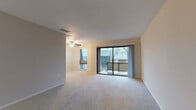 This single-floor residence offers a thoughtfully designed layout that balances comfort and functionality. The living area is generously proportioned, featuring soft wall-to-wall carpeting, neutral tones, and a ceiling fan that contributes to the room's airy feel. Large sliding glass doors open onto a private balcony, allowing abundant natural light to fill the space while providing pleasant views of the surrounding neighborhood and mature trees. A secondary window further enhances the brightness of the living area.

The kitchen is efficiently arranged, showcasing white cabinetry with silver hardware, dark speckled countertops, a stainless steel sink, and tile flooring. Ample upper and lower cabinet storage makes this kitchen both practical and organized, with a dishwasher integrated seamlessly into the cabinetry.

The bedroom is a calm and comfortable retreat, finished with plush carpeting, a ceiling fan with integrated lighting, and a large window with blinds that frames an outdoor view. A bifold closet door opens to reveal a well-sized closet with a hanging rod, providing convenient storage.

The bathroom is clean and bright, featuring tile flooring, a white vanity with under-sink storage, a large mirror with overhead lighting, and a tub-shower combination. Throughout the residence, neutral color palettes and consistent finishes create a cohesive and inviting atmosphere.